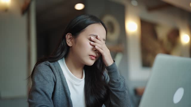 An Asian woman is feeling headaches and eye pain after working for hours