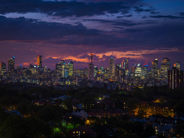The image captures the captivating skyline of downtown Sydney at twilight, with clouds in the sky tinted with shades of pinkish-purple and deep blue, creating a tranquil and dreamy ambiance. The brightly lit buildings of the city reflect its prosperity and modernity. Viewed from a distance, the city’s night is filled with charm and vitality.
