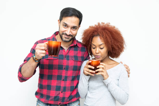 Smiling and happy heterosexual couple standing together with red coloured coffee mugs