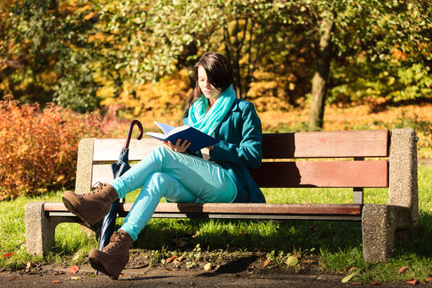 Fall lifestyle concept. Casual young woman girl relaxing in autumnal park reading book. Golden colorful leaves background