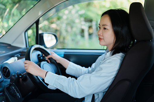 Young Asian woman seating at the driver's seat of a right hand drive vehicle, smiling