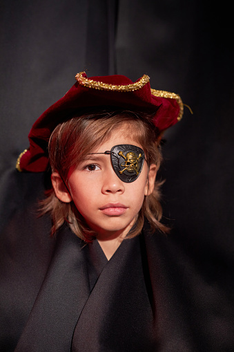 Front view closeup of little boy wearing pirate costume peeking from curtain on stage in theater