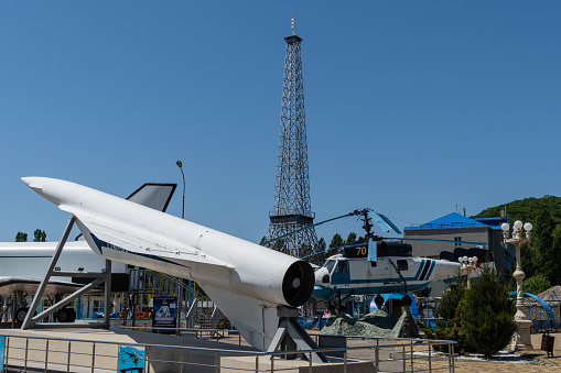 Ka-25 helicopter and Soviet cruise missile in front of model of Eiffel Tower in Arkhipo-Osipovka. Layout of Eiffel Tower against blue sky. Krasnodar Territory, Russia - May 14, 2021.