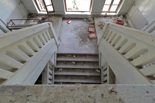 Two flight of stairs with intermediate half landing inside the remains of a ruined, abandoned former primary school building from AD 1948, full of rubble with peeling walls. Vevcani-North Macedonia.