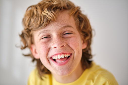 Smiling kid in yellow outfit with brown wavy hair looking at camera in daylight