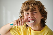 Boy with grimace cleaning teeth on light background