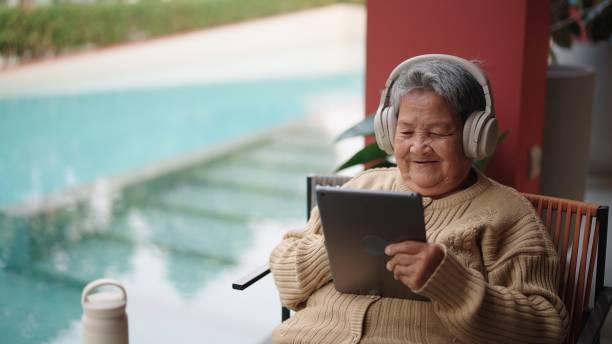 Senior woman using digital tablet. Asian senior woman using digital tablet at poolside of hotel resort. old woman smiling tablet stock pictures, royalty-free photos & images