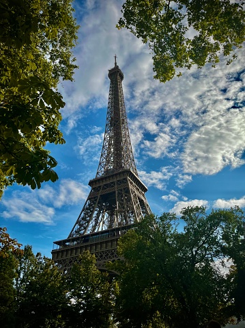The Eiffel Tower under blue cloudy sky with trees in front