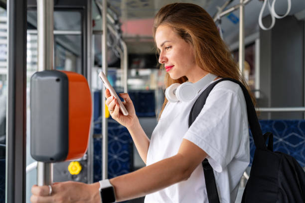 istock Brunette woman in white tee shirt standing inside bus and using her smart phone. 2012538267