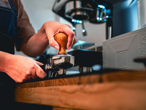 Close-up of hand Barista cafe making coffee with manual presses ground coffee using tamper at the coffee shop