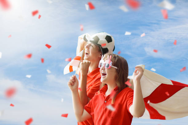 England football supporter on stadium. English fans on soccer pitch watching team play. Group of British supporters with flag and national jersey cheering for UK. Championship game. Go Britain!