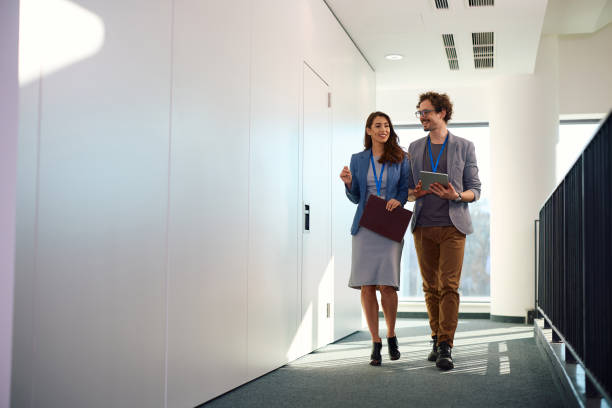 istock Happy business colleagues talking while walking through hallway of an office building. 2012561865