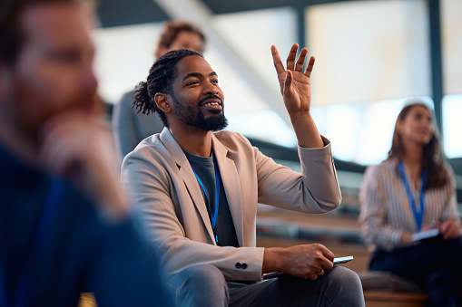 African American entrepreneur raising his arm to ask a question during a  business conference in board room.