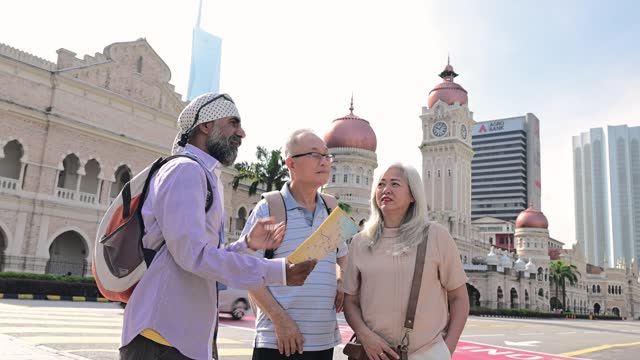 Senior Sikh tour guide explaining the history of the heritage Sultan Abdul Samad Buildings to two senior Asian traveler at the Merdeka Square, Kuala Lumpur
