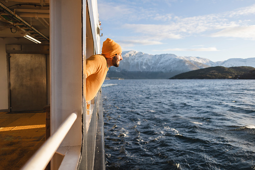 Handsome man leaning on the railing of the ferry while crossing the fjords at sunset