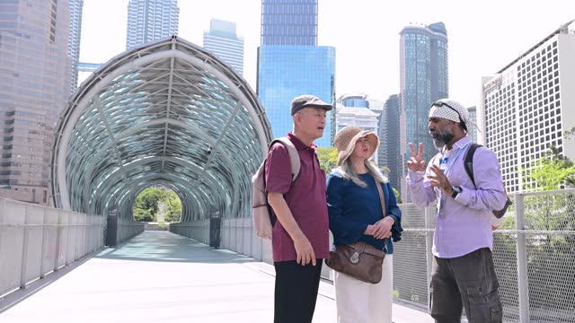 A private Sikh tour guide and two senior Asian traveler walking through the famous Saloma Bridge landmark in the city of Kuala Lumpur, Malaysia