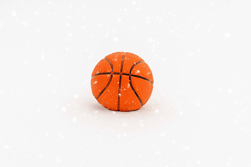 Orange basketball ball lie on the snow close-up copy space.
