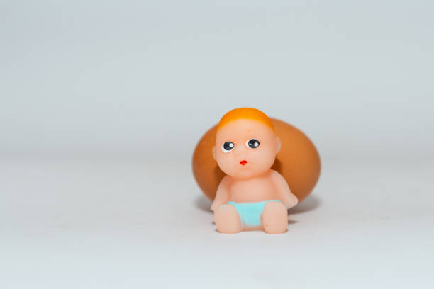 Miniature newborn baby toy and egg sitting on a white gray background.Selective focus,copy space.