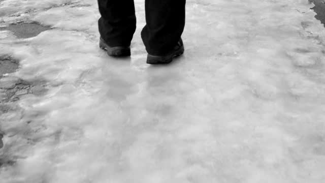 the legs of a man walking on an icy sidewalk on a winter evening, rear view 4k video