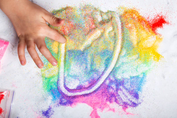 Kid playing with colorful sand on white background. Motor skills, child creativity concept