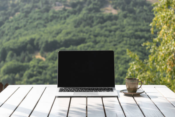 istock Laptop computer with copy space on black screen and coffee cup on table in outdoor cafe of mountain resort. Online work and relax, travel, online education, distance learning, alternative office 2012638872