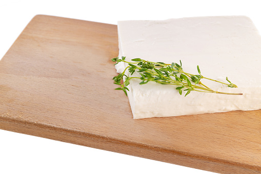 Tofu cheese with thyme on a wooden board isolated on a white background. Curd cheese on a cutting board.