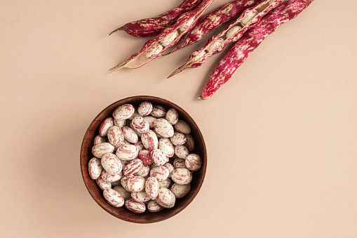 Cranberry beans. Borlotti bean pods in bowl. Top view. Stylish modern food background. Magenta color. Creative foodstuff flat lay. Grocery, dietary backdrop. Advertising, trendy magazine publication. Raw dry red bean. Crimson beans. Snap. White red pods.