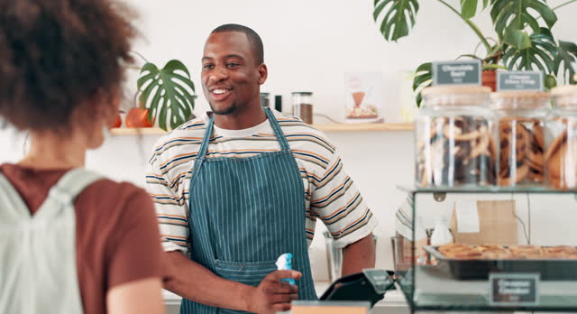 Cashier, customer service and order at counter with cafe questions, menu choice and hospitality in small business. Happy African barista, people or waiter working, talking and helping at coffee shop