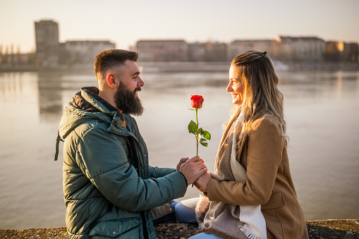 Man giving red rose to his woman while they enjoy spending time together outdoor.