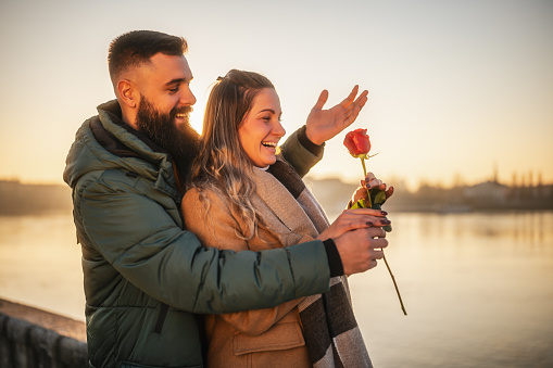 Happy man giving red rose to his woman while they enjoy spending time together on a sunset.