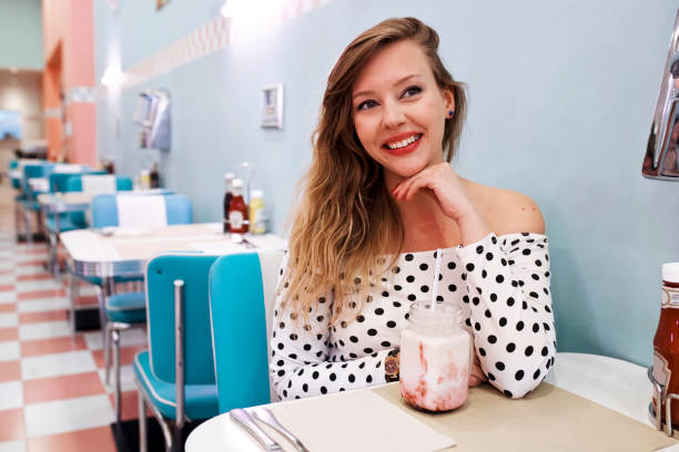 Two people sipping milkshakes and sharing a meal at retro-themed diner, capturing warm ambiance and cheerful interaction