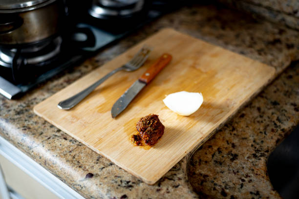 Wooden cutting board with knife, fork, meat and onion on top. Lunch preparation.