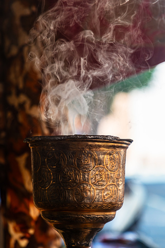Incense burning in metal, cup shape, ornamental incense burner at arabic souk in Oman. Close up shot with focus on smoke.