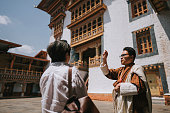 Bhutanese tour guide explaining Bhutan history to Asian tourist in front of Punakha Dzong