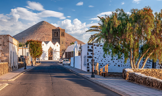 Experience the serene beauty of La Candelaria Church in La Oliva, Fuerteventura, nestled under a majestic mountain in a historic Canarian village.