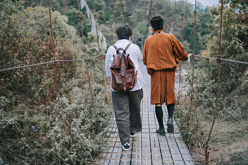 Asian female tourist crossing hanging footbridge with Bhutanese tour guide at iron bridge of Paro River, Bhutan
