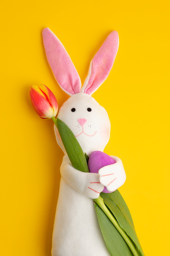 A cute felt Easter Bunny folding a fresh tulip and an Easter egg.