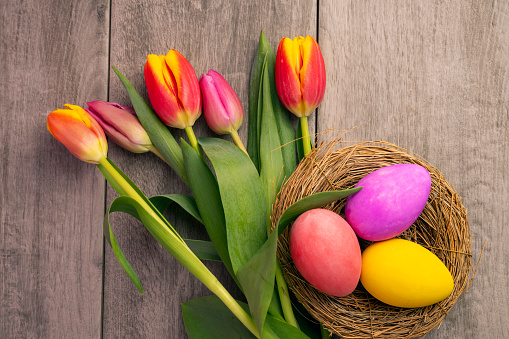 A nest with colored Easter eggs with tulips blurred in the background.