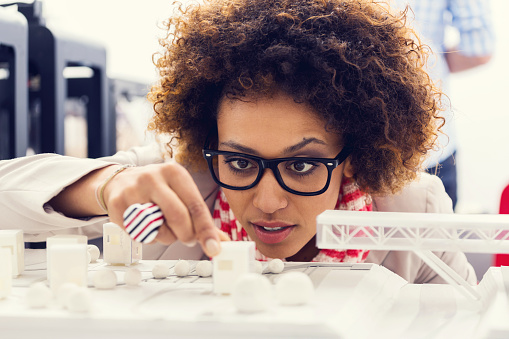 Close up of mixed race young architect sitting in a 3D printer office and watching 3D printings.