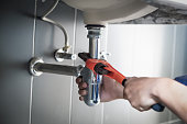 Plumber uses wrench to repair water pipe under sink There is maintenance to fix the water leak in the bathroom.with red wrench, plumbing install concept.