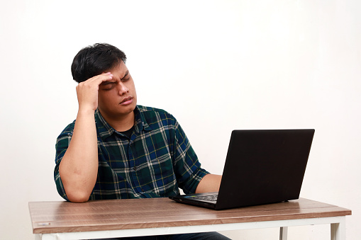 Stressed young asian college student having headache while sitting with laptop on the desk
