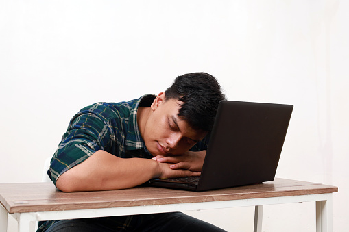 Tired young asian man sleeping while sitting with laptop on the desk