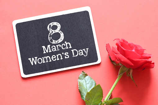 March 8, Women's Day words on a chalk board on a red background next to a red rose.