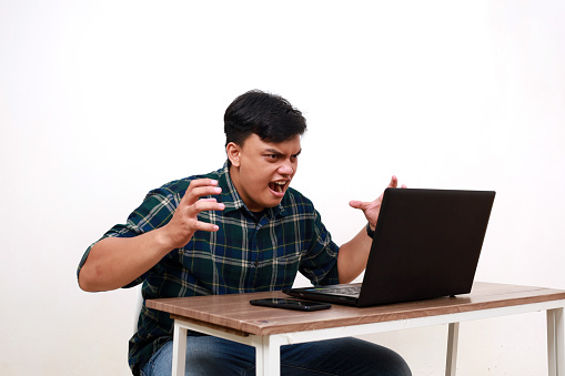 Young asian man using a laptop with angry face expression and gesture