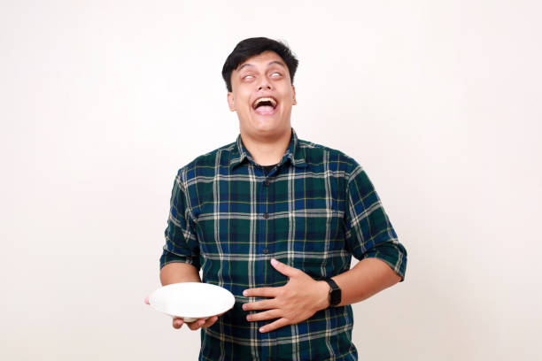 istock Satisfied Young asian man feels full, touching his stomach while holding an empty plate 2012835719