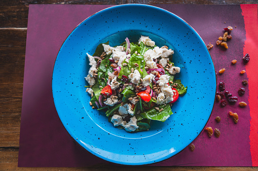 Mixed ingredients in the plate, meal salad with spinach and goat cheese, chopped vegetables and sunflower seed