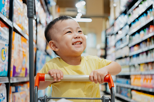 Little Asian Chinese boy pushing small shopping cart buying food and snacks in supermarket