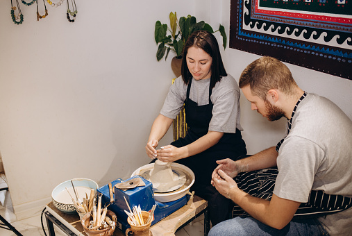 Romantic caucasian couple working on potter wheel. Handsome man and pretty beautiful brunette woman making and sculpting clay pot together and hugging.