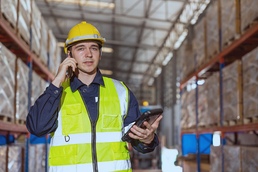 Warehouse worker using smartphone phone calling contact people in factory cargo storage area.