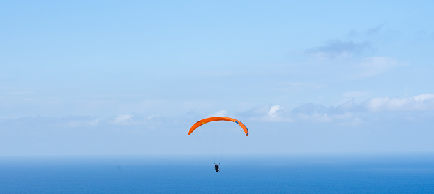 Two people riding a tandem paragliding over the sea